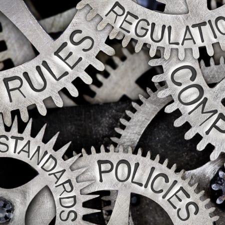 Macro photo of tooth wheels with COMPLIANCE, REGULATIONS, STANDARDS, POLICIES and RULES words imprinted on metal surface